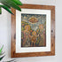 A framed religious cuzco painting depicting the Holy Family (Mary, Joseph, and the child Jesus) under a cloudy sky, housed in a rustic brown wooden frame with a white mat, hanging on a light gray wall with green leaves in the foreground.