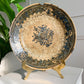 An antique ceramic Safavid plate with a blue floral pattern and crackle glaze, displayed on a gold-colored stand on a white surface with a green plant in the background.