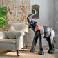 Decorative antique leather elephant figure in a living room setting with a floral curtain and white sofa.
