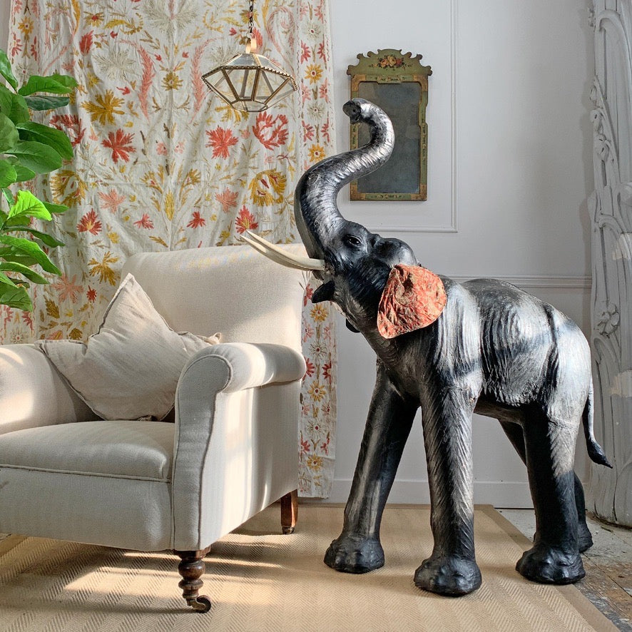 Decorative antique leather elephant figure in a living room setting with a floral curtain and white sofa.