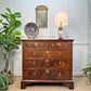 An outstanding quality two short over three long English chest of drawers dating to the reign of George II, the Walnut veneer marquetry on Walnut frame, Oak lined with 'Running Dog' Parquetry work around each drawer surround in Holly veneer, styled in a classic room setting with a potted plant, a decorative plate, a wall mirror, and a table lamp.