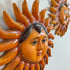 A close-up of a handcrafted Sergio Bustamante sun wall hanging with a human face and radiating sun rays, shown against a plain light background. A second similar sun decoration is partially visible in the upper right.