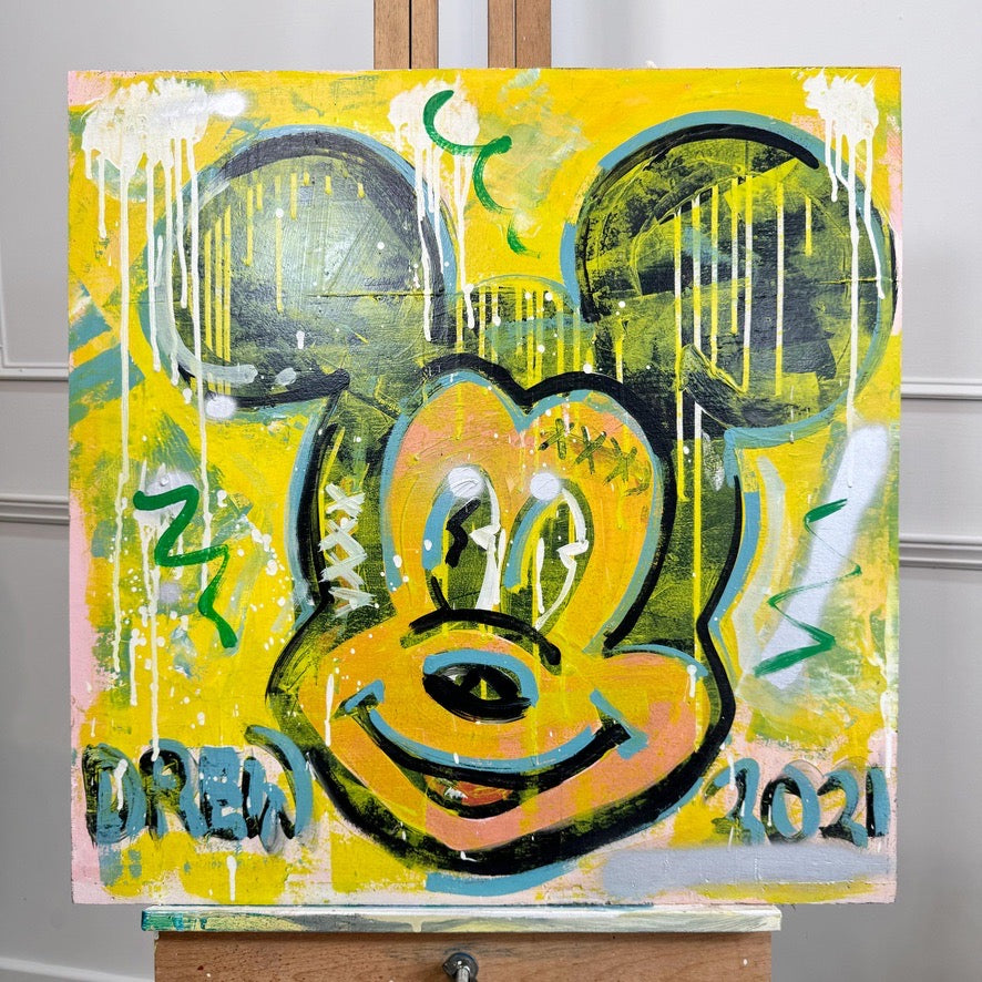 A square canvas painting on an easel featuring a stylized Mickey Mouse face in yellow, black, green, and blue with dripped paint effects and the text 'BREW 2021' on a light gray wall background.