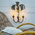 A decorative faux bamboo palm wall sconce with a palm tree motif and three candle-style lights, mounted on a white paneled wall above a rattan chair.