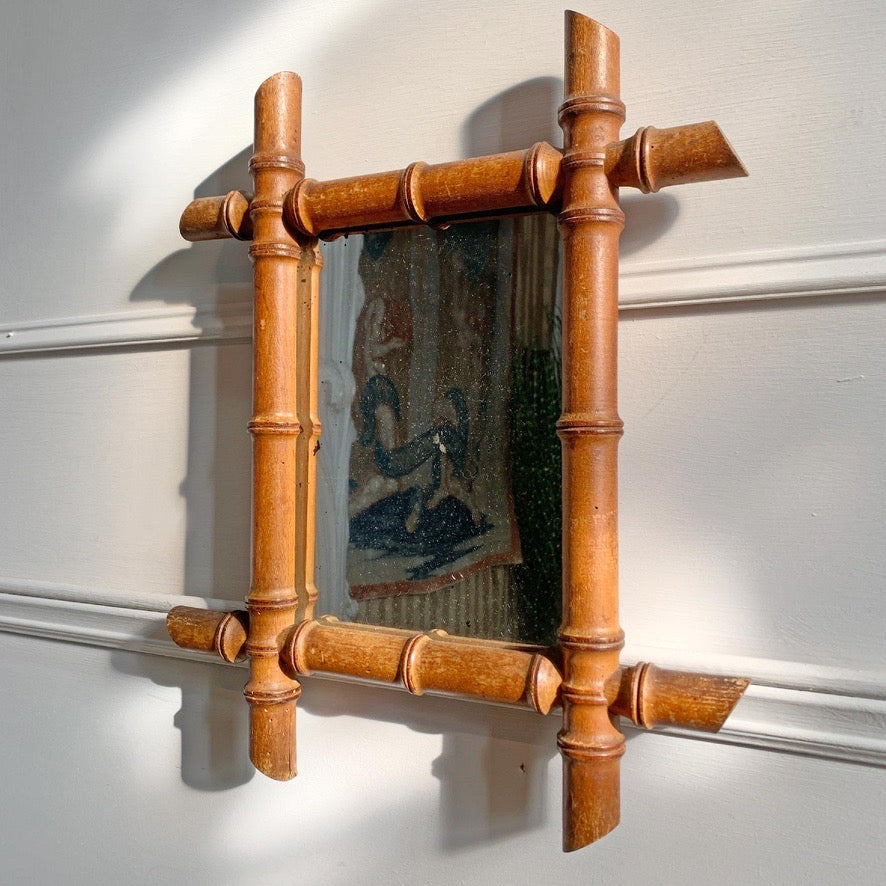 A rectangular  vintage French wall mirror with a decorative bamboo frame, mounted on a white paneled wall. The mirror reflects a colorful tapestry