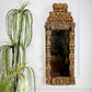An ornate, antique Italian rectangular wall mirror with a highly carved, sculpted golden wooden frame, shown hanging on a white paneled wall next to a green potted plant.