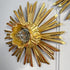 A gold antique wooden chapel church 
sunburst wall sconce with a clear glass shade, mounted on a white wall.