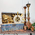 An antique distressed blue wooden chest with a carved gold lion head, displayed next to two tall turned wooden candlesticks on a rustic wooden table against a plain white wall.