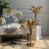 Decorative banana palm tree table lamps in brass metal beside a patterned armchair in a styled interior setting.