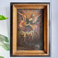 A framed antique Cuzco religious painting depicting  Archangel Michael defeating Satan, mounted on a light gray wall with a green plant leaf visible on the left.
