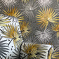A close-up of a patterned fabric or wallpaper featuring stylized palm fronds in metallic gold, white, and dark gray on a dark gray background.