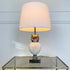 A Willy Daro vintage table lamp with a large cream-colored drum shade, a textured white owl-shaped ceramic base, and a gold-toned metal head, displayed on a glass-topped side table against a white paneled wall.