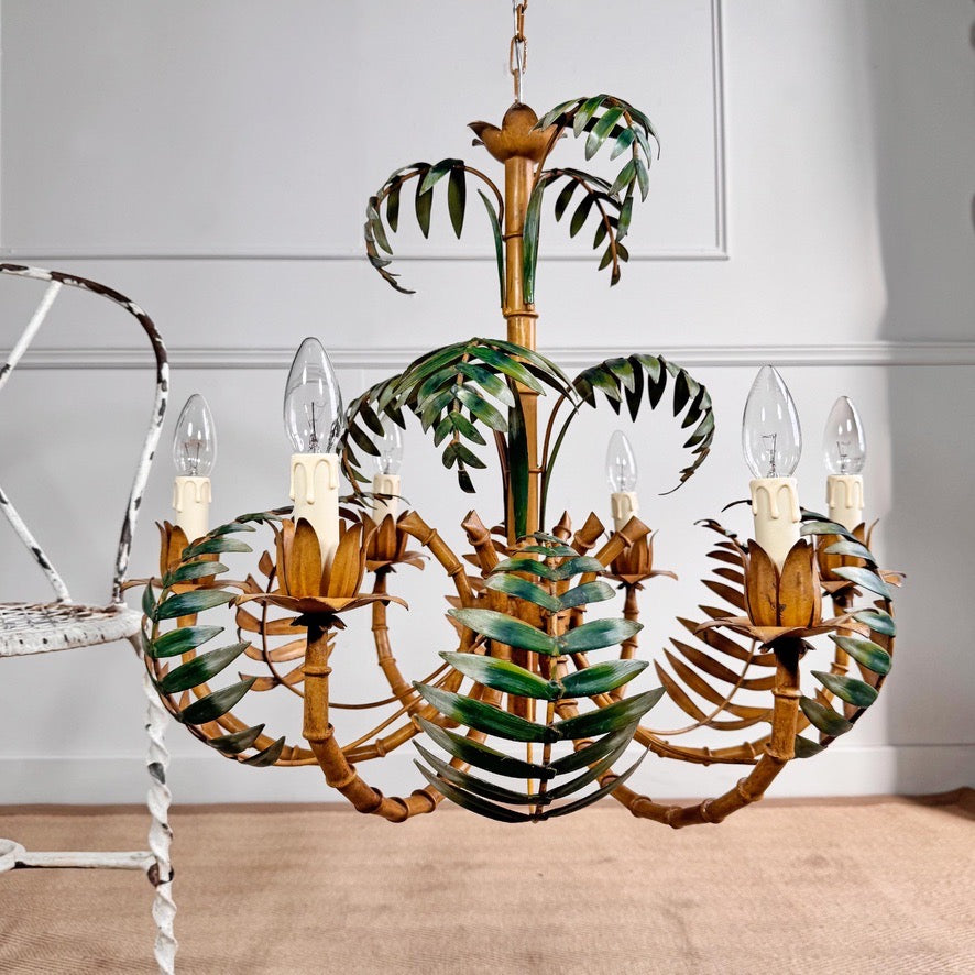 A tropical faux bamboo palm tree vintage Italian chandelier with a toleware metal frame, green painted leaves, and candle-style light sockets, shown hanging in a room setting.