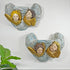 Two decorative Plaster CherubPutto Wall Shelves Circa 1920 wall-mounted angel and clouds sculptures with blue-gray draped forms and gold wings, shown against a plain white wall with a small green plant leaf at the lower left.