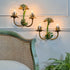 Two decorative vintage toleware wall sconces with faux bamboo and palm-leaf details in green and gold, mounted on a white paneled wall above a woven-back chair.