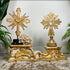 An antique ornate carved wooden religious gold and white carved decorative stand displayed on a  floor against a white wall, with green plants framing the scene and a coral piece between the crosses.