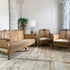 An antique Chinoiserie bergere three-piece furniture set featuring an ornate carved, hand painted gold wooden sofa, two matching armchairs, and a small side table with a lamp, set in a classic room with stone floors and white columns.