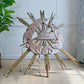A decorative wooden all seeing eye religious sculptural , surrounded by many radiating gold wooden sunburst rays.  photographed indoors on a light beige floor against a pale wall, with a plant leaf visible at left.