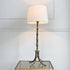 Mid Century Brass Faux Bamboo Table Lamp in the manner of Maison Bagues France, shown lit on a glass-topped side table against a white paneled wall.