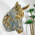 An antique zinc wall-mounted horse head sculpture with a distressed gray finish and gold leaf accents, shown against a white wall with potted green plants on the right.