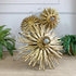 Gold sunburst wood and gesso wall decor with three flower-like spheres and central light bulbs, styled on a beige surface with potted ferns and a white chair in the background.