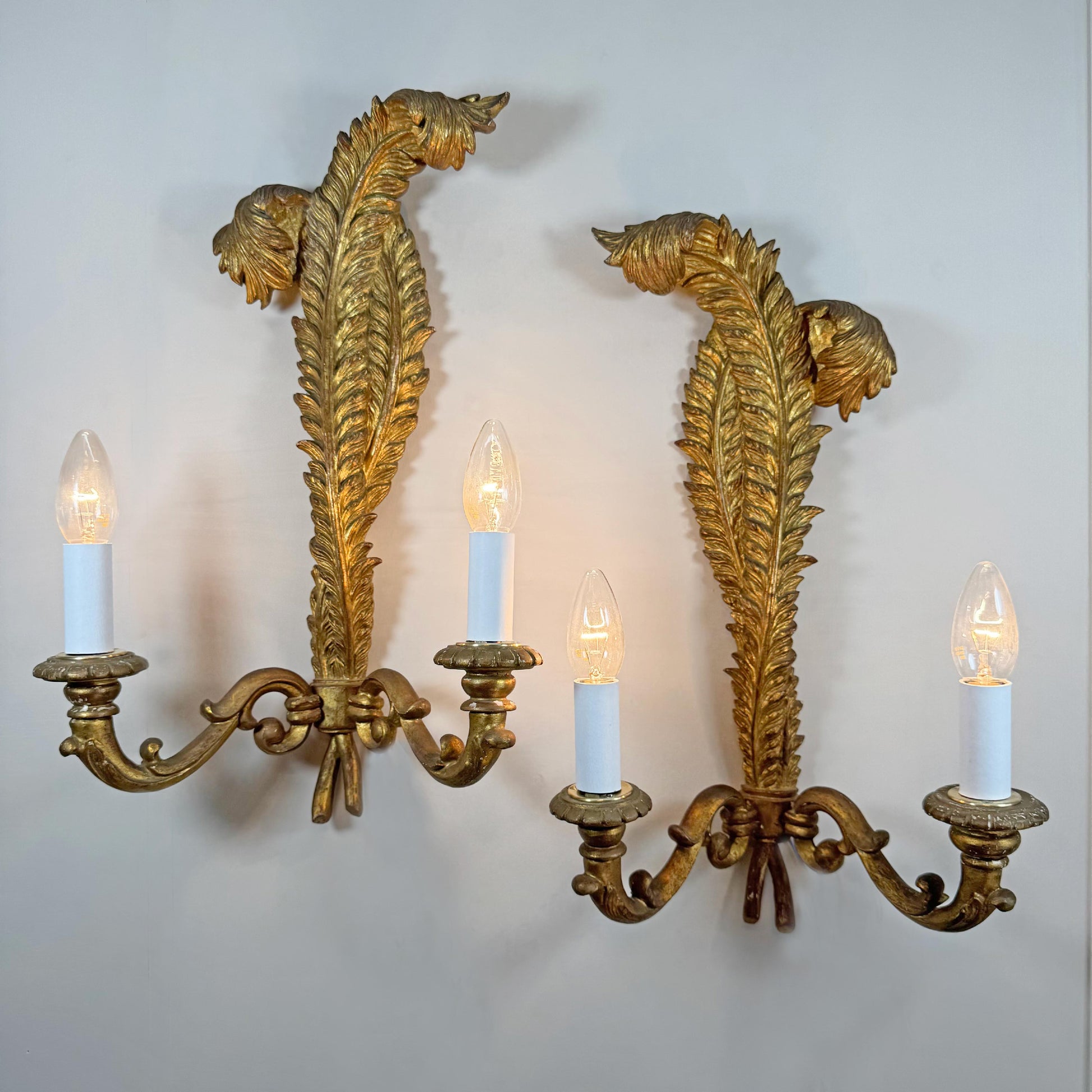 A pair of ornate Italian antique gold wall sconces with leaf-like scrollwork and four candle-style lights, mounted on a plain light gray wall.
