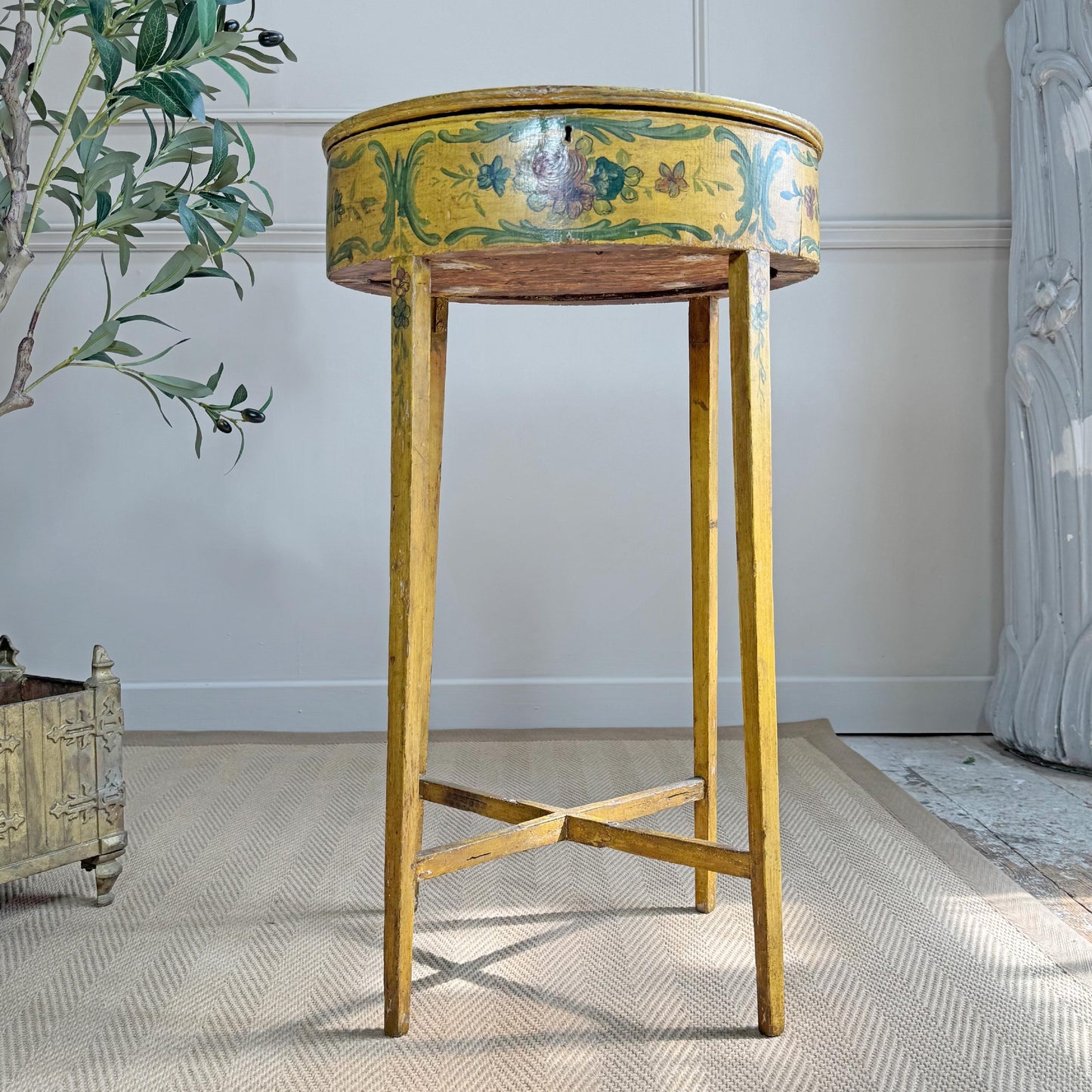 A vintage Italian Venetian oval side table with a distressed yellow painted finish and hand-painted floral motifs, set on a textured beige rug in a styled room.