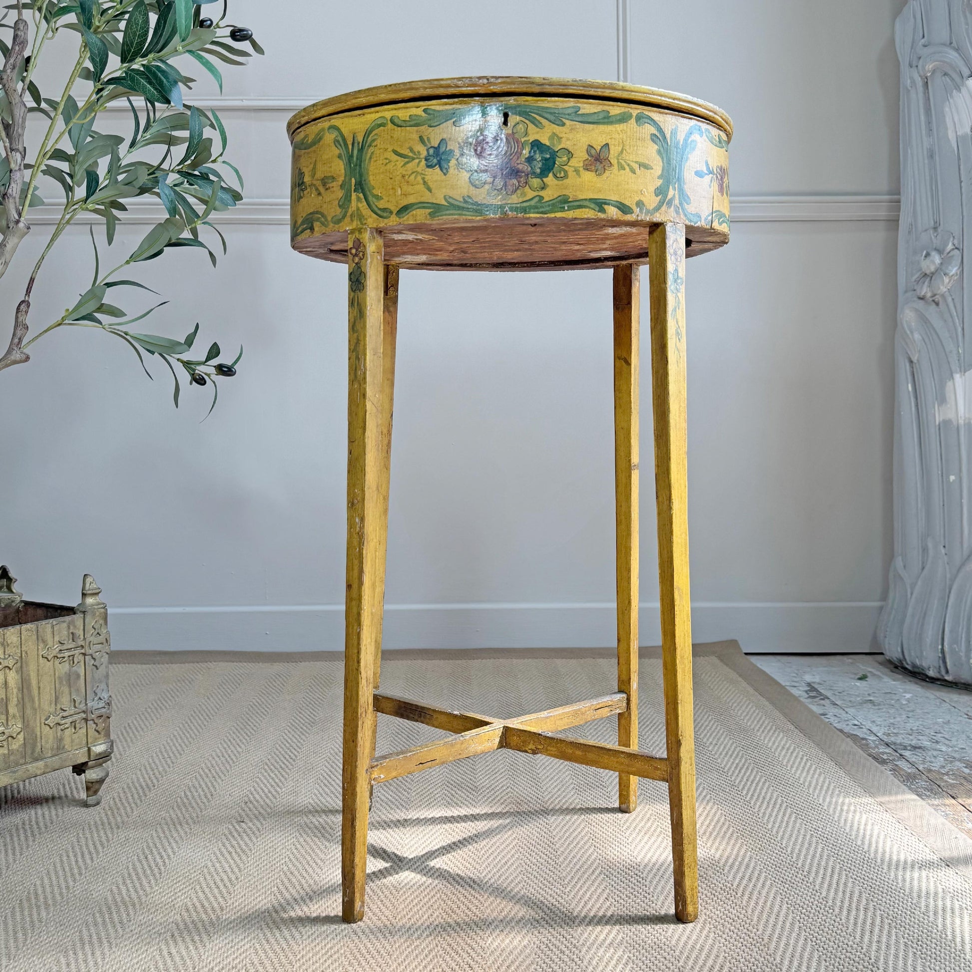 A vintage Italian Venetian oval side table with a distressed yellow painted finish and hand-painted floral motifs, set on a textured beige rug in a styled room.