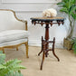 A small round antique swedish wooden pedestal side table with ornate turned legs and a dark carved apron, styled in a room next to a cream upholstered armchair with a coral sculpture on top.s