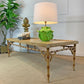 A rectangular console table with a bamboo-style frame and a light wood top, styled in a room setting with a lamp, decorative objects, and a potted plant.