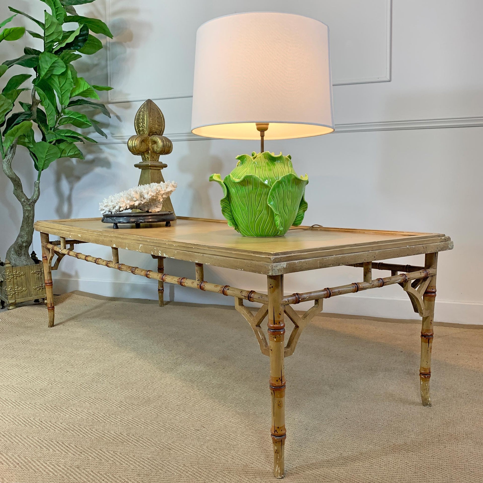 A rectangular console table with a bamboo-style frame and a light wood top, styled in a room setting with a lamp, decorative objects, and a potted plant.