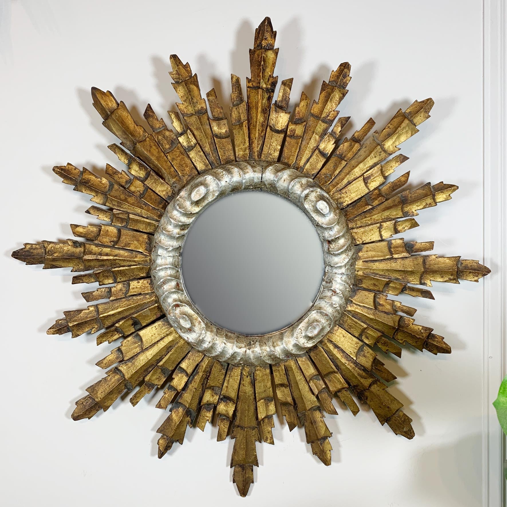 A decorative sunburst wall mirror with a distressed gold-painted frame and a silver-toned beaded border around the circular mirror, mounted on a plain white wall.