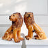 Two glossy ceramic Staffordshire lion figurines in warm tan and brown tones, posed side by side on white pedestals against a white paneled wall.