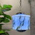 A hanging blue marble glass pendant light with a faceted light blue glass shade featuring dark brown and black marble-like veining, suspended by a silver-toned chain in an indoor setting with a plant and wall decor visible.