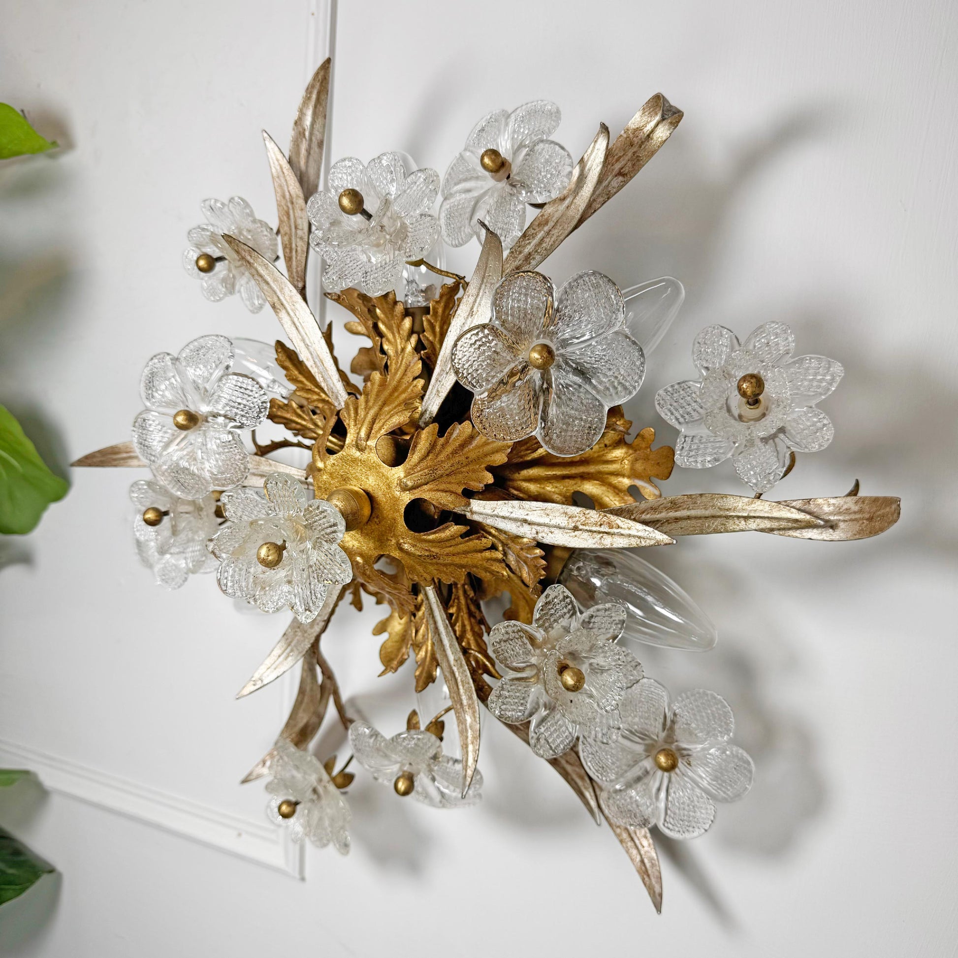 An ornate Banci Firenze vintage wall sconce featuring a gold-painted central acanthus leaf cluster, clear textured glass flower petals, and metallic gold leaf-like leaves, mounted on a white wall.