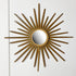 A Chaty Vallauris gold sunburst wall mirror with a circular mirror center and radiating metal rays, mounted on a plain white wall.