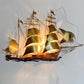 A decorative Daniel D'haeseleer Gold Galleon Wall Light C 1970's metal wall light shaped like a three-masted sailing ship, with illuminated gold-toned sails and a warm brown hull, mounted against a plain light wall.