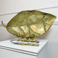 A large David Marshall  leaf-shaped serving tray or dish in a metallic gold finish with raised vein details, displayed on a white pedestal with a pair of matching gold-handled nutcrackers in front.