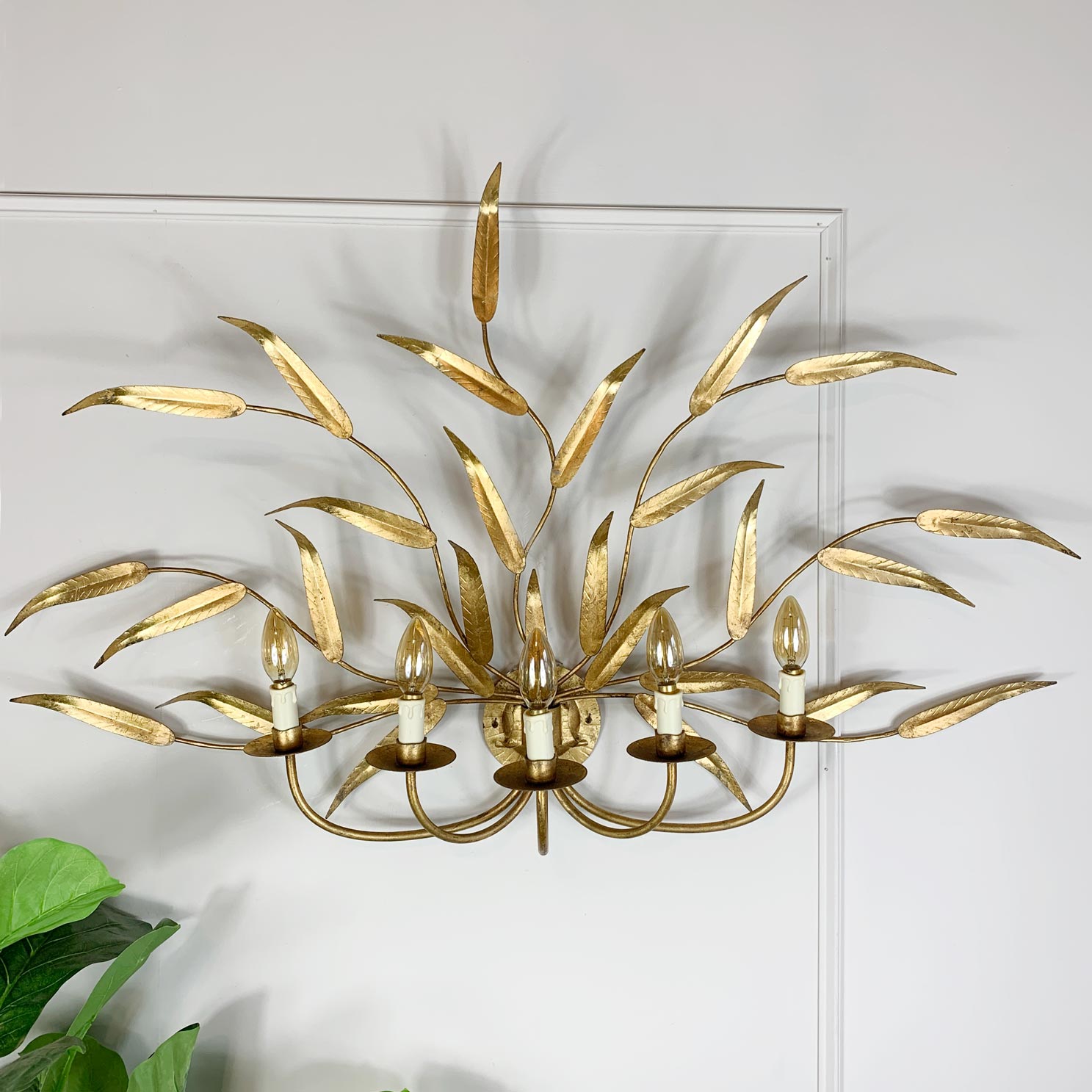 A gold leaf-shaped wall sconce with multiple candle-style lights, mounted on a white wall.