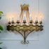An ornate vintage Spanish Ferro wall-mounted half chandelier shaped light with a crown-shaped top, six candle-style bulbs, and a distressed gold/bronze metal frame mounted on a white wall.