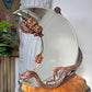 A Gabrielle Viardot ornate round wall mirror with a carved bronze dragon head at the top and a dragon body wrapping around the base, displayed on a wooden surface in an indoor setting.