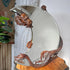 A Gabrielle Viardot ornate round wall mirror with a carved bronze dragon head at the top and a dragon body wrapping around the base, displayed on a wooden surface in an indoor setting.