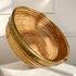 A round woven rattan Crespi basket with a natural tan color and a polished brass rim, displayed on a white surface against a white paneled wall.