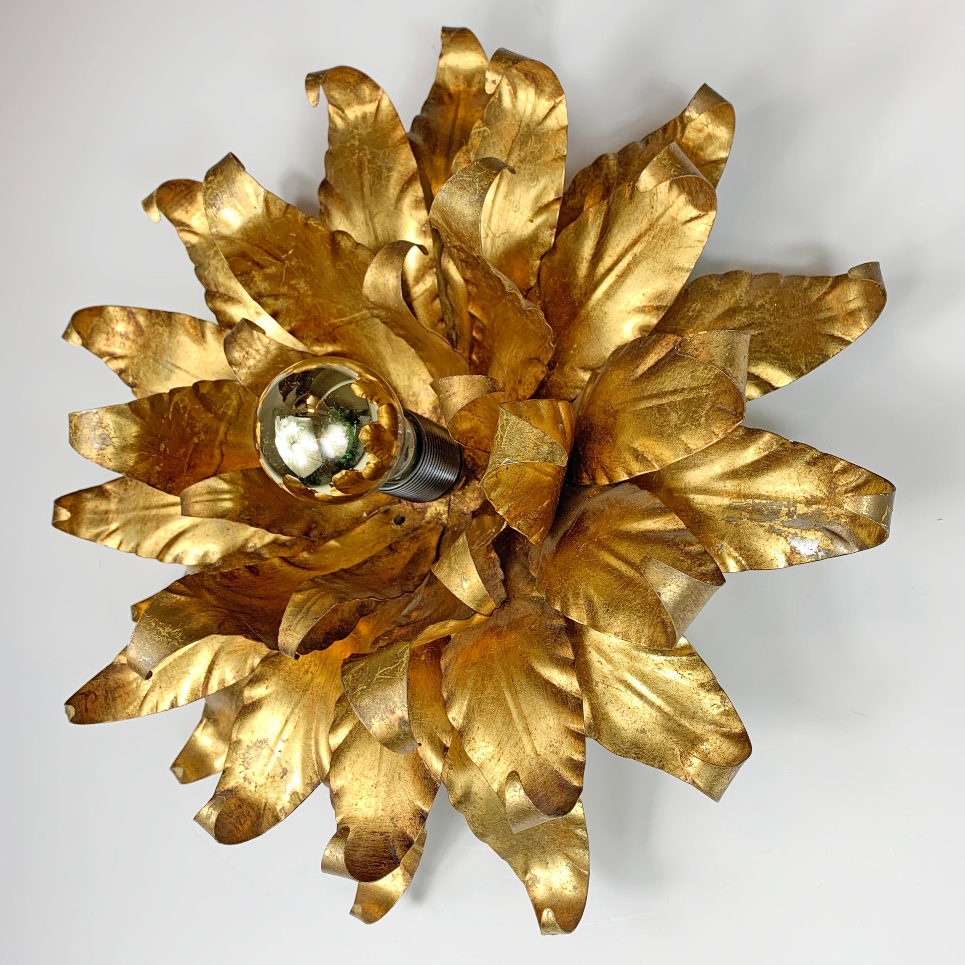 A gold leaf flower shaped wall sconce with a single bulb visible in the center, photographed against a plain light background.