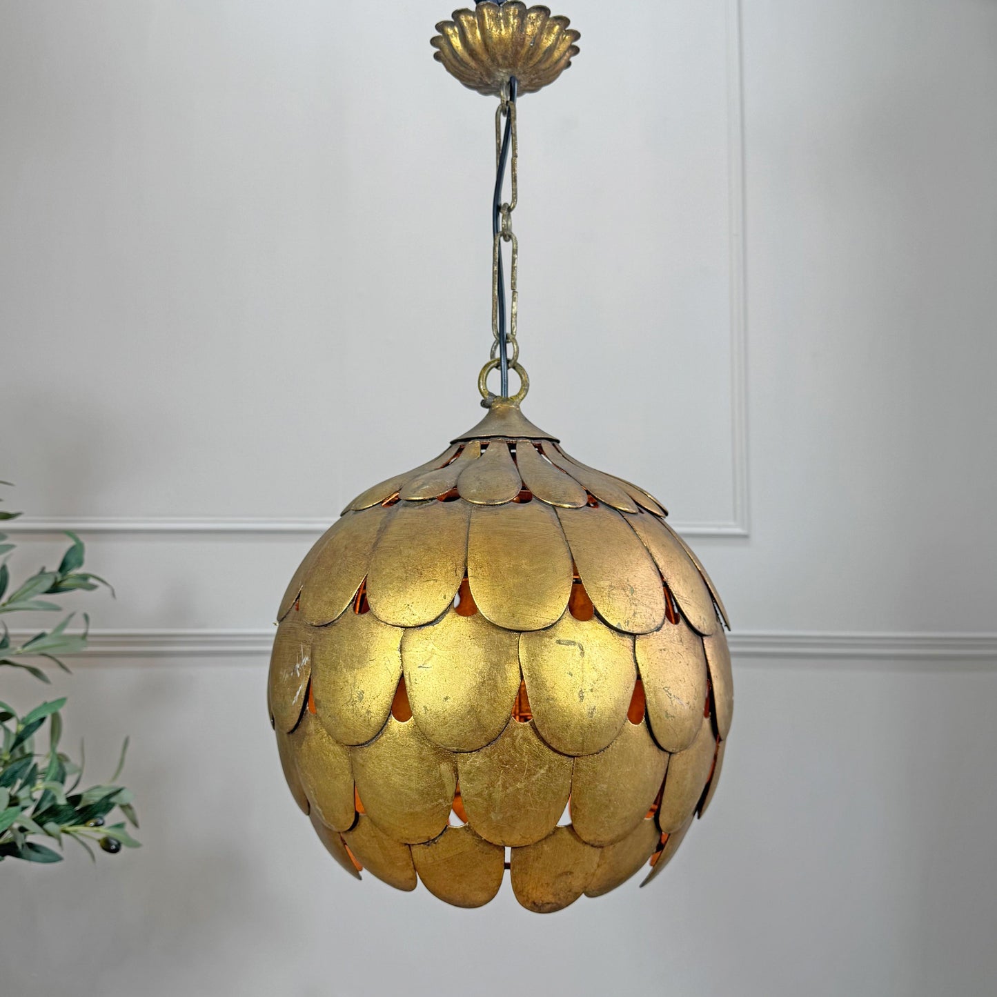A vintage-style Salvadori gold pendant light with a scalloped, petal-like shade suspended from a matching gold ceiling canopy, shown against a white paneled wall with a small plant visible at the left edge.
