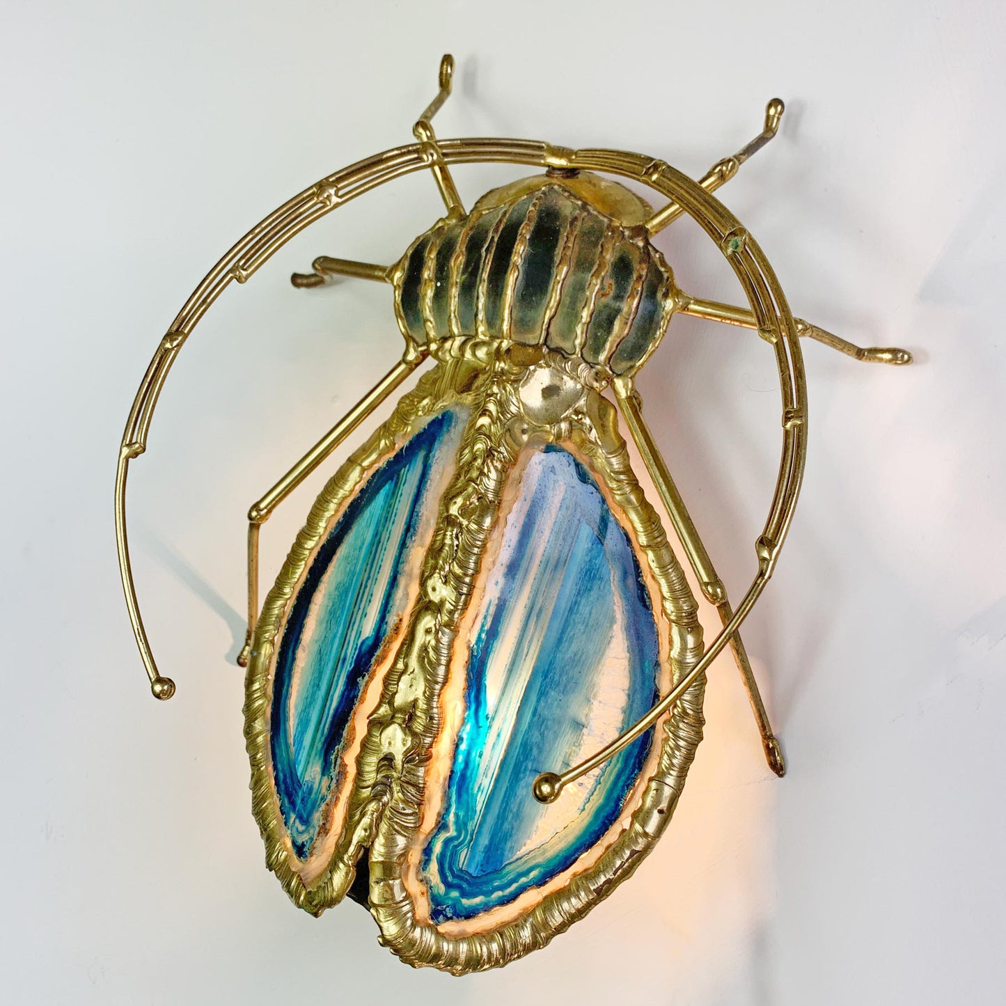 A Henri Fernandez Illuminated Gold Blue Agate Sculpture of a Longhorn Beetle beetle wall light with a gold metal frame and wings featuring blue, teal, and cream marbled patterns, shown against a plain white background.