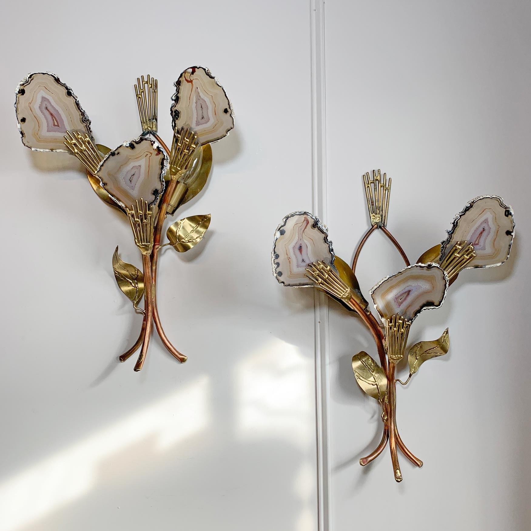 A pair of Henri Fernandez Signed Agate and Brass Wall Lights mounted on a white wall. Each sconce features three petals made from agate slices with gold-toned fronds and leaves, attached to copper-toned stems.