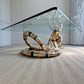 A modern Isabelle Faure snake-head coffee table with a clear glass rectangular top and a sculptural base coiled like a snake, featuring metallic gold, bronze, and black bands, set on a textured beige rug.