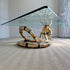 A modern Isabelle Faure snake-head coffee table with a clear glass rectangular top and a sculptural base coiled like a snake, featuring metallic gold, bronze, and black bands, set on a textured beige rug.