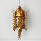 An ornate antique-style gold metal lantern pendant chandelier hanging against a white wall.